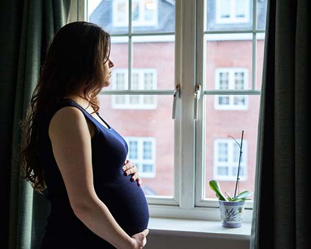 pregnant woman looks out window holding her belly thinking about adoption choices for her child